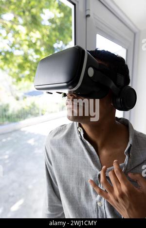 Biracial man using vr headset next to window at home Stock Photo
