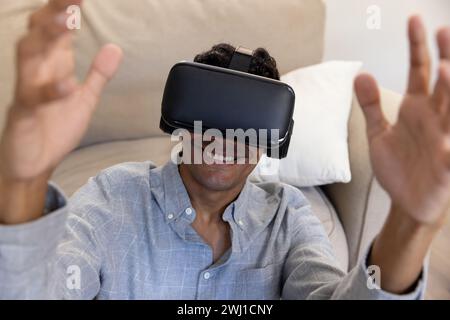 Happy biracial man using vr headset touching virtual screen at home Stock Photo