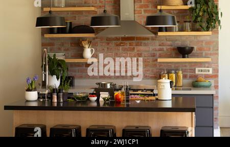 Domestic kitchen with shelves and hood over hob on exposed brick wall and hanging lamps over island Stock Photo