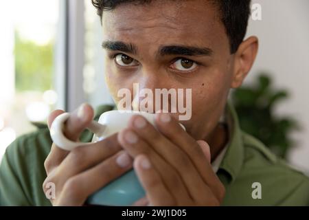 Portrait of biracial man holding mug and drinking coffee at home Stock Photo