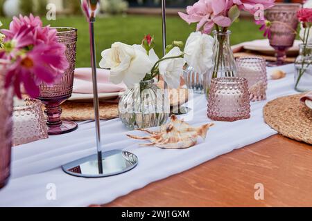 Pink picnic aesthetic table setting, flowers arrangement, shells close up. Cozy setup with flowers and candles. Stock Photo