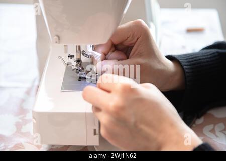 Woman's hand in front of the sewing machine to thread the needle and then sew. Precision and minute detail. Stock Photo