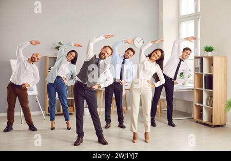 Happy smiling young business people doing stretching exercises in office together. Stock Photo
