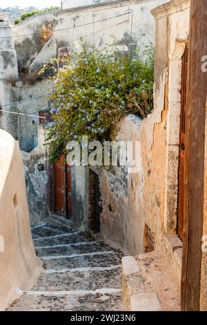 Typical narrow stone stepped lane between weathered rustic walls and brown wooden doors in the small town of Exo Gonia on the Greek island, Santorini. Stock Photo