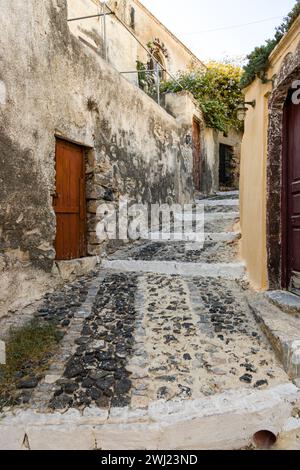 Typical narrow stone stepped lane between weathered rustic walls and brown wooden doors in the small town of Exo Gonia on the Greek island, Santorini. Stock Photo