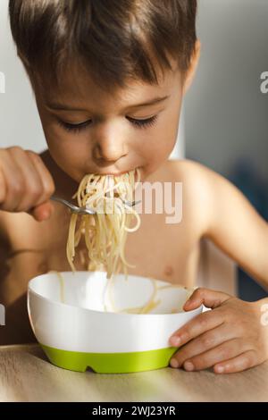 Cute toddler boy eating his favorite food - Spaghetti Stock Photo