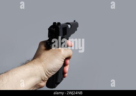 First person view of male hand with black pistol isolated on gray background Stock Photo