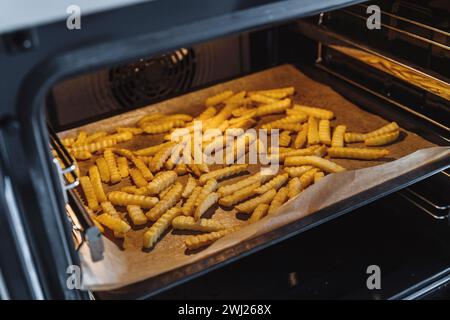 Crispy French fries spread out on an oven tray, lined with baking paper Stock Photo