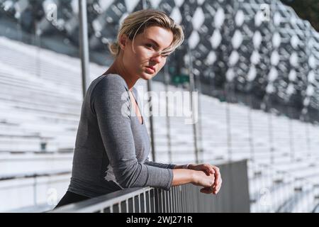Portrait of confident woman athlete wearing female sportswear on bleachers in outdoor stadium Stock Photo