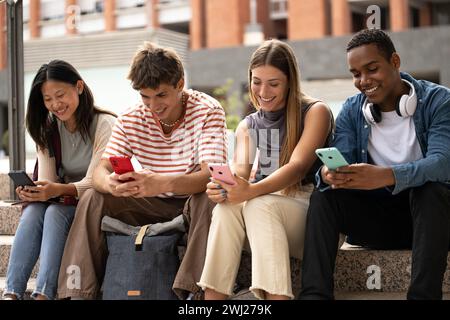 Multiracial young people sitting in stairs while texting.Cheerful group of friends using their phones in the street. Stock Photo