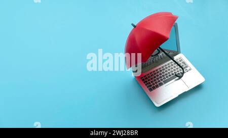 Computer and network security concept. Red umbrella cover the laptop over a blue background. Stock Photo