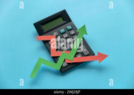 red and green arrow graph on calculator over a blue background. Stock Photo