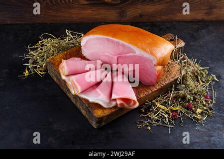 Traditional South Tyrolean farmer's ham sliced and in one piece offered with dried herbs as a close-up on a rustic cutting board Stock Photo