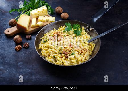 Traditional AllgÃ¤uer KÃ¤sespÃ¤tzle with walnuts served as close-up in an iron frying pan on a rustic board Stock Photo