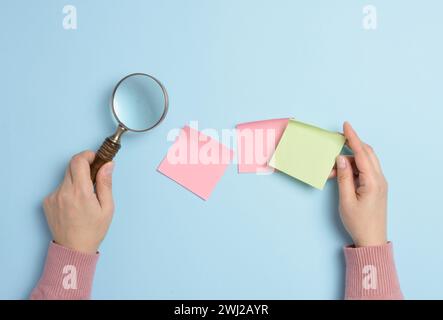 Empty paper stickers adhered to a blue background, and a female hand with a magnifying glass on a blue background Stock Photo
