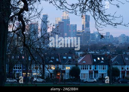 Seen through the branches of trees in Ruskin Park are the lit windows of terraced period homes and in the distance, the growing development at Nine Elms, on 10th February 2024, in London, England. Stock Photo