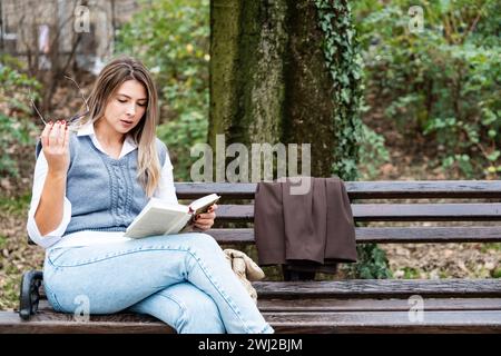Young businesswoman taking a break from work sitting in the park relaxing while reading a book. Business female office worker read outdoor during lunc Stock Photo