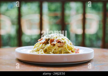 A plate of Spaghetti Carbonara with mushroom and meat garnished with herbs and grated cheese on top. Placed on a wooden surface. Stock Photo