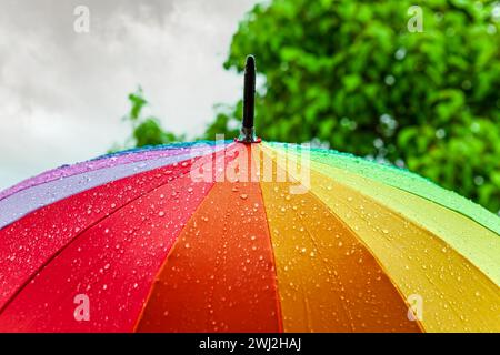 Rain On Rainbow Umbrella. Umbrella under heavy rain against cloudy sky background. Rainy weather Stock Photo