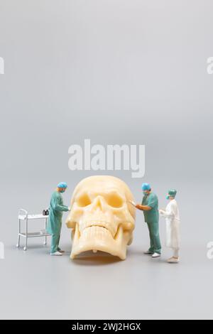 Miniature people Doctor with a giant human skull on a grey background Stock Photo