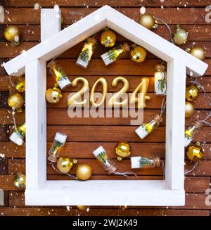 House key with keychain cottage on festive brown wooden background with stars, lights of garlands. New Year 2024 wooden letters, Stock Photo