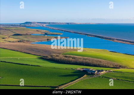 Abbotsbury, Dorset, UK.  12th February 2024.  UK Weather.  Aerial view across fields at Abbotsbury in Dorset looking along Chesil Beach and the Fleet lagoon to the Isle of Portland on the Jurassic Coast on a warm sunny afternoon.  Picture Credit: Graham Hunt/Alamy Live News Stock Photo