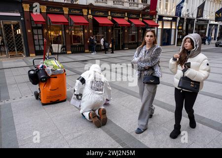 People pass by a man on Bond Street wearing white overalls and a Black Lives Matter sign sticks letters down onto the pavement in a protest with an unclear message on 4th February 2024 in London, United Kingdom. Stock Photo
