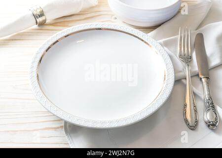 Preparation for a place setting with a white plate, napkin and nostalgic silver cutlery on a light-colored wooden table for fest Stock Photo
