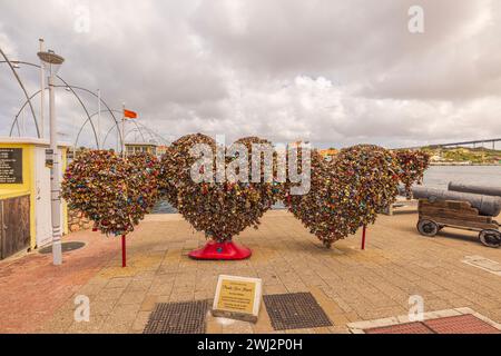 A beautiful view of three heart symbols installed on the promenade adorned with hanging padlocks tells tales of eternal love. Willemstad. Curacao. Stock Photo