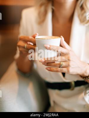 Woman with a cup of coffee sits in a chair, leaning on the handrail. Cropped. Faceless Stock Photo