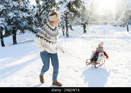 Mother and her cute little son having on a sledding hill during sunny winter day Stock Photo