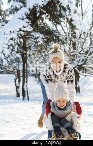 Mother and her cute little son having on a sledding hill during sunny winter day Stock Photo