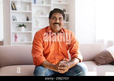 Positive middle aged eastern man sitting on couch at home Stock Photo