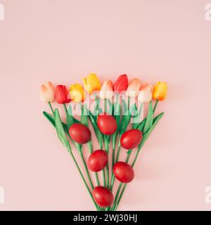 Creative Easter and spring composition made with red Easter eggs and various colorful tulips on light pastel pink background. Minimal Easter concept. Stock Photo