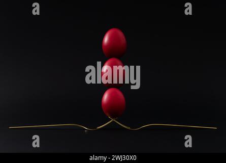 Creative Easter holiday composition made with red colored eggs balancing on golden forks against black background. Minimal Easter concept. Stock Photo