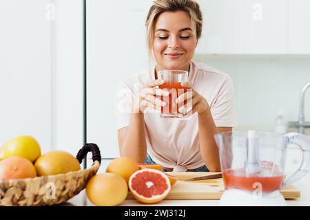Woman drinking freshly squeezed homemade grapefruit juice in white kitchen Stock Photo