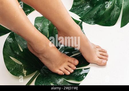 Wet female feet with smooth skin and Monstera deliciosa tropical leaf Stock Photo