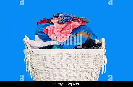 Wooden basket with dirty laundry on blue background. Clothes in rattan basket. multicolored dirty Stock Photo