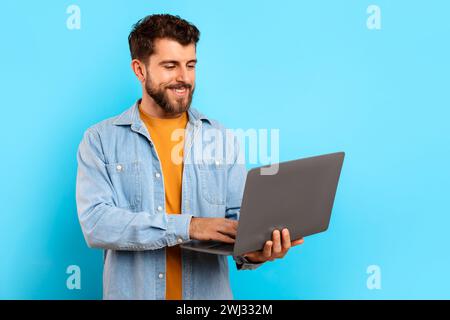 Happy young man typing on his laptop websurfing in studio Stock Photo