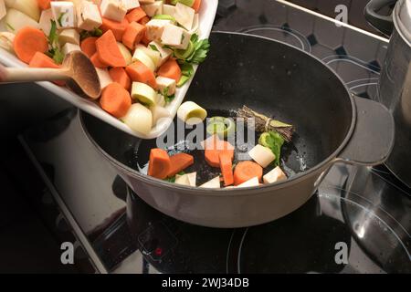 Diced vegetables are poured into an oval casserole pot on the stove top to roast them for a sauce, stock, soup or stew, cooking Stock Photo