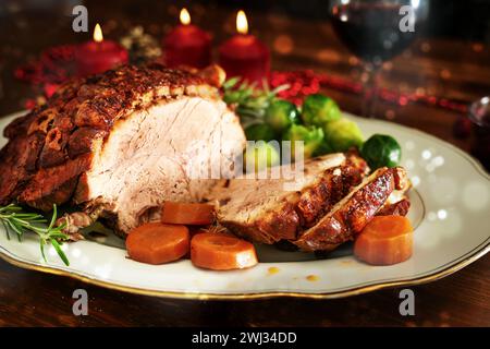 Christmas ham or roast pork with crispy fat crust, served with vegetables on a dark wooden table with candles and bokeh bubbles, Stock Photo