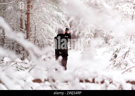 Middle aged hiker in winter forest taking a photo with his mobile phone. Man taking selfie in snowy forest with blurred out background Stock Photo