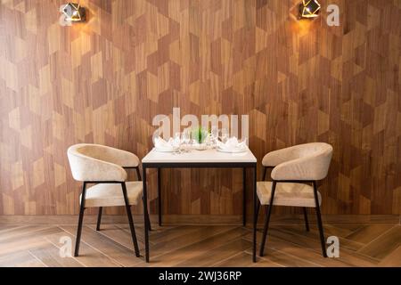 Table set up for two in a cafe, cafeteria, restaurant. Table and two chairs stand against the wall. Empty seats for visitors. A place for a date, a ro Stock Photo