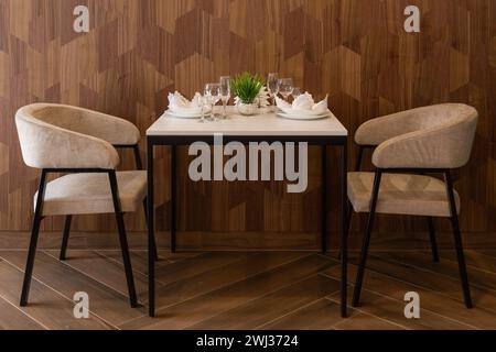 Table set up for two in a cafe, cafeteria, restaurant. Table and two chairs stand against the wall. Empty seats for visitors. A place for a date, a ro Stock Photo
