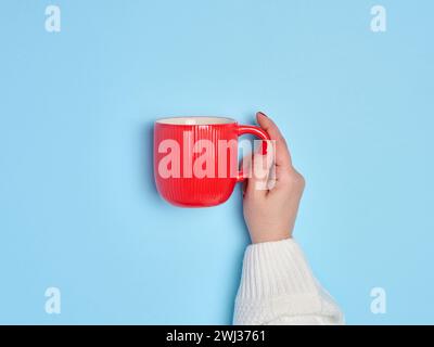 Female hand holding a red ceramic cup on a blue background Stock Photo