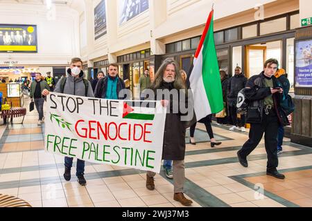 Leeds, UK. 12 FEB, 2024. Pro Palestine demonstrators march through Leeds Station waving flags and banners. A large banner reads 'Stop the Genocide, Free palestine' Credit Milo Chandler/Alamy Live News Stock Photo