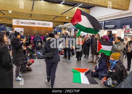 Leeds, UK. 12 FEB, 2024. Pro palestine protestor waves palestinian flag infront of other demonstrators in main throughfare for Leeds train station. Credit Milo Chandler/Alamy Live News Stock Photo