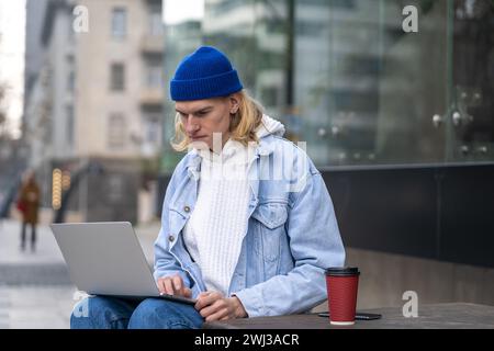 Serious focused freelancer IT guy engrossed in laptop remote work on urban outdoor space on street. Stock Photo