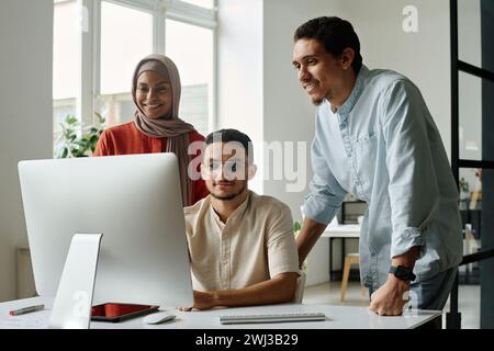 Team of young Muslim brokers or analysts looking at computer screen and discussing online data or points of new business project at meeting Stock Photo