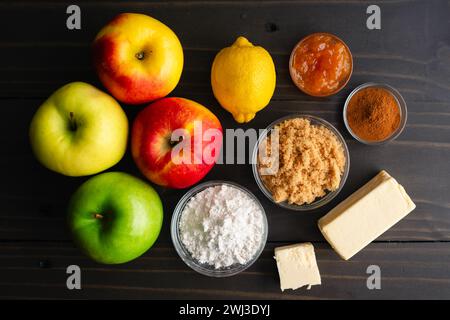 Vegan Apple Tart Ingredients on a Wooden Table: Fresh apples, flour, brown sugar, vegan butter, and other pastry ingredients on a dark background Stock Photo